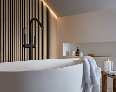 SlatWall Waterproof on wall behind white bath with black tap. Strip lighting to highlight the wood effect texture.