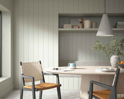 Green Tongue and Groove wall panelling in a dining room with a neutral table, two-tone woven chairs and grey accessories.