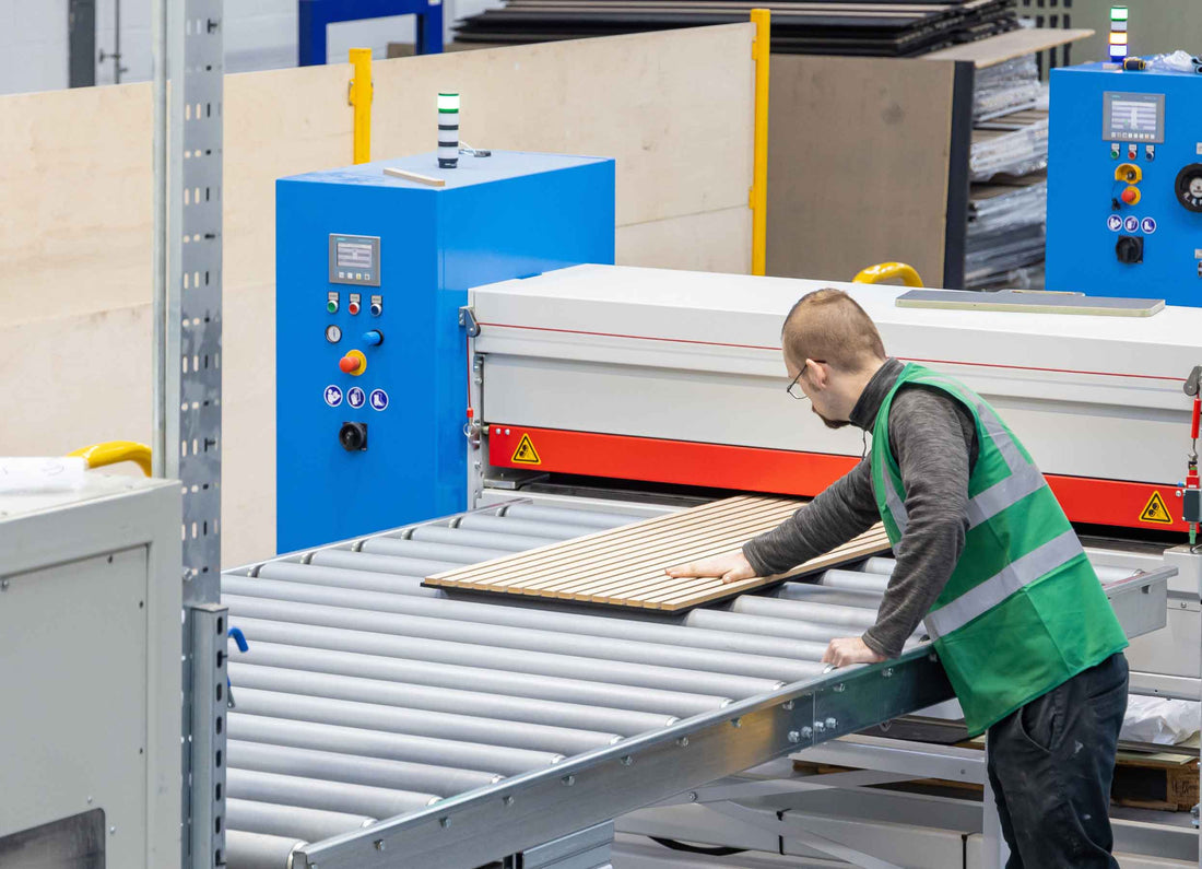 A man with his hand on top of a SlatWall Natural Oak panel on the adhesive bonding line in Naturewall's factory.