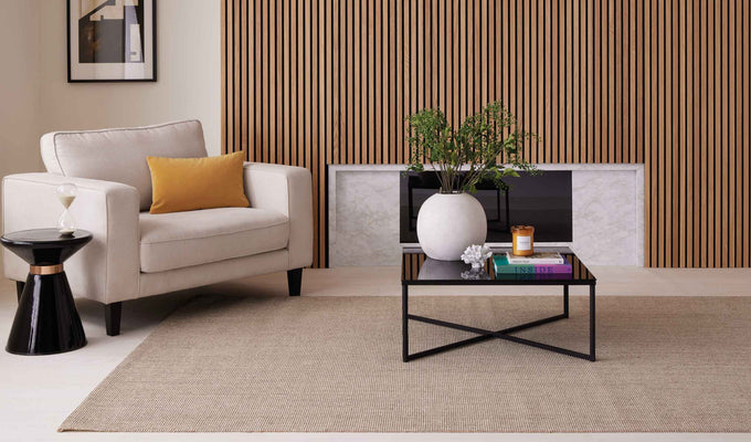 Living room wall panelling idea with oak wood panels above a fireplace, a cream chair, black tables and amber accessories.
