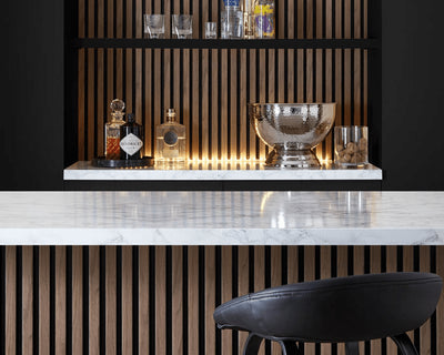 This image shows a kitchen island with the SlatWall behind the shelves and a bar stool. The shelves display bottles of alcohol and an ice bucket 
