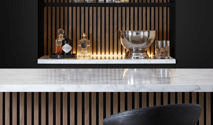 This image shows a kitchen island with the SlatWall behind the shelves and a bar stool. The shelves display bottles of alcohol and an ice bucket 