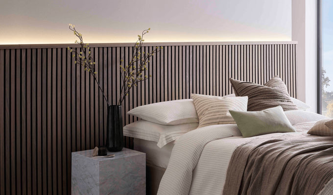 SlatWall Midi Walnut panels and coordinating Top Trim behind a marble side table and a white bed with various cushions.