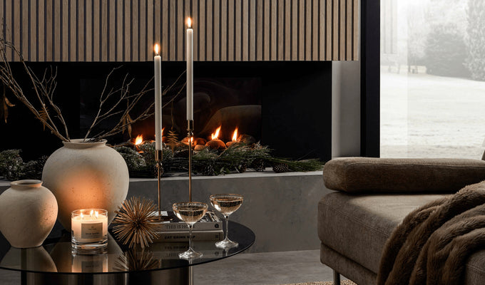 This image shows a fireplace with a SlatWall covering, in front of the fire there is a coffee table with lit candles, two glasses or champagne and some Christmas ornaments. The corner of a sofa can be seen also.