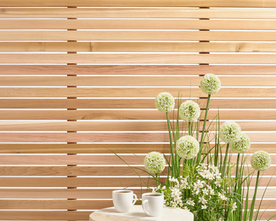 Cedar wood outdoor panels behind green and white flowers next to a table with two coffee cups.
