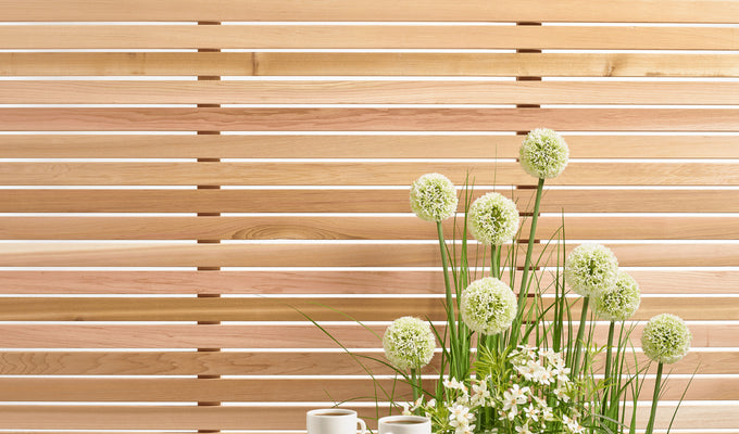 Cedar wood outdoor panels behind green and white flowers next to a table with two coffee cups.