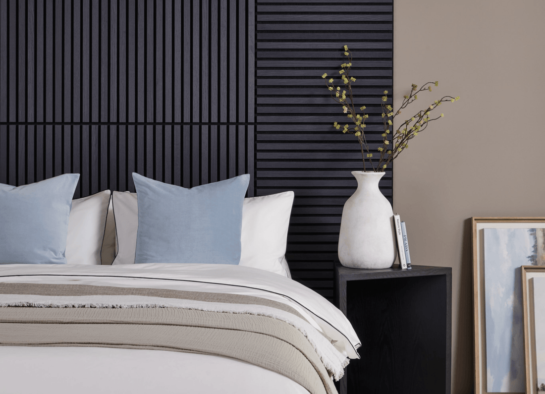 A white bed featuring blue cushions in front of a bed headboard design made with SlatWall Mini Charcoal Black panels.