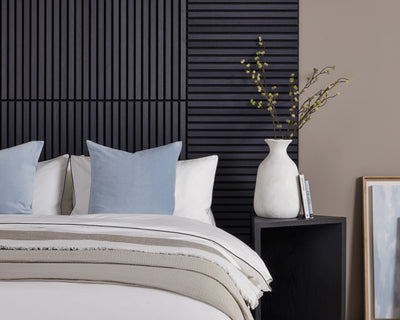 A white bed featuring blue cushions in front of a bed headboard design made with SlatWall Mini Charcoal Black panels.