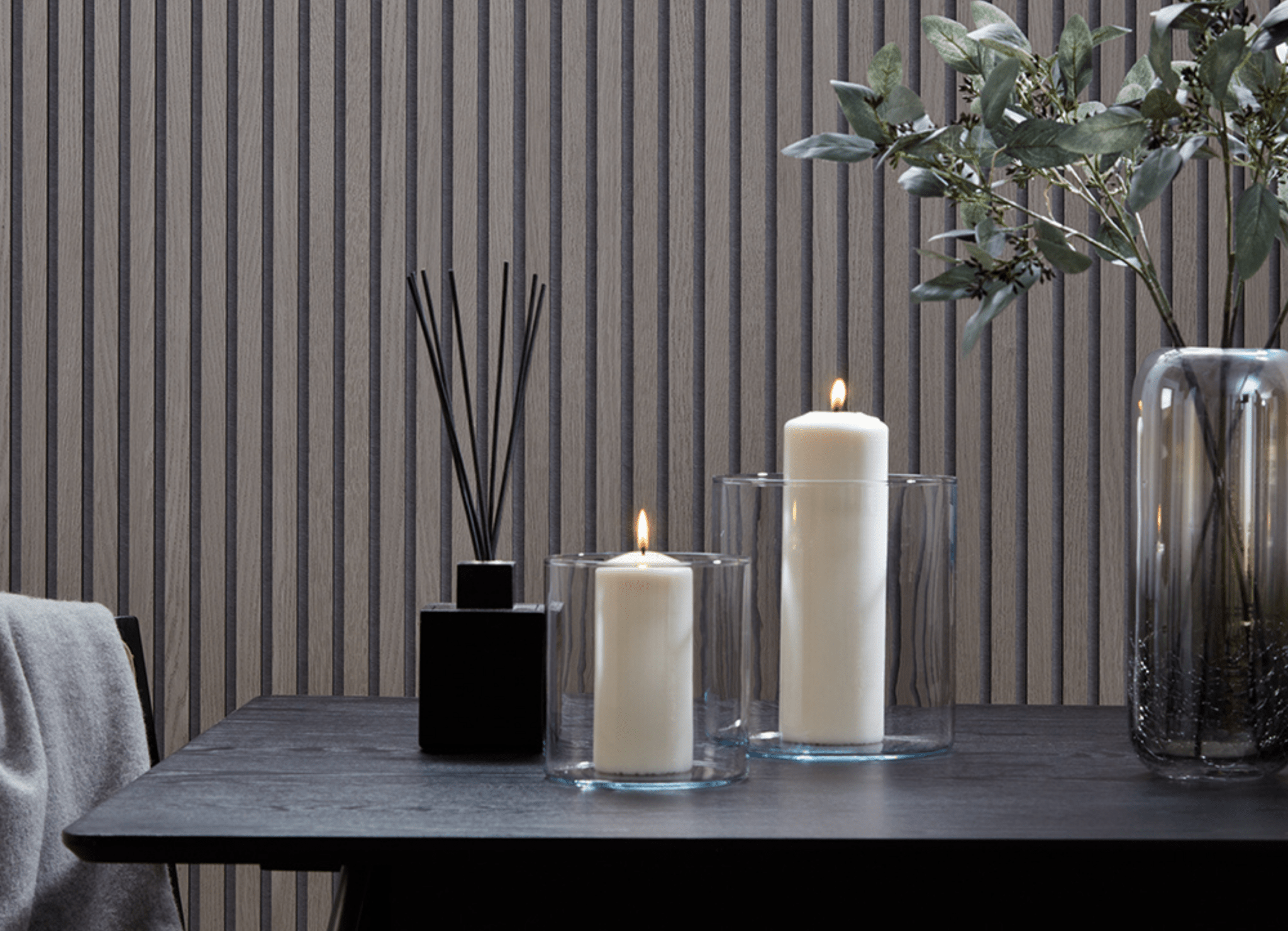 Greige interior design featuring SlatWall Grey Oak panels and a black table with two lit candles, a reed diffuser and vase