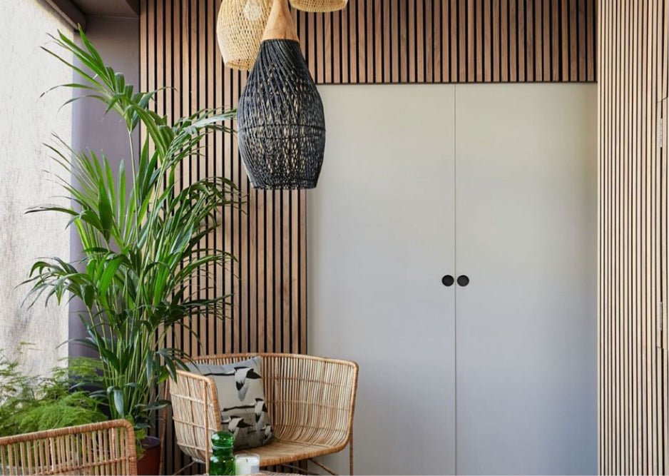 White double doors surrounded by Naturewall Natural Oak on black felt SlatWall panels. Rustic wicker chairs and greenery in foreground.