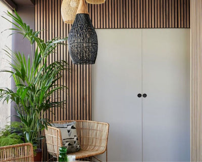 White double doors surrounded by Naturewall Natural Oak on black felt SlatWall panels. Rustic wicker chairs and greenery in foreground.