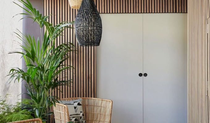 White double doors surrounded by Naturewall Natural Oak on black felt SlatWall panels. Rustic wicker chairs and greenery in foreground.
