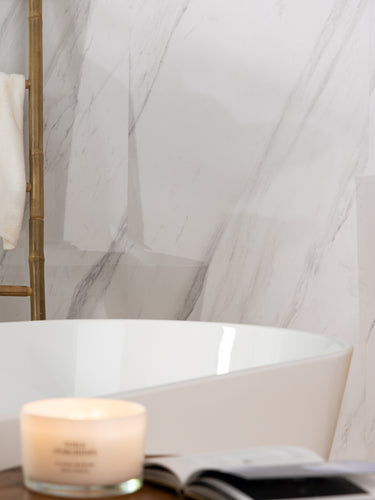 Elemence Shower Panels Calacatta White close up of grey marbling. Corner of bath with candle and book