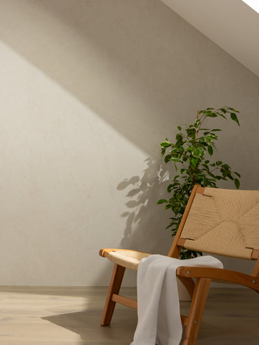 Elemence Shower Panels Chalk Beige on wall with shadow. Wooden chair in front and plant.