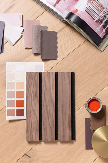 Mood board showing a Walnut SlatWall Grand sample from Naturewall on table with pot of paint, paint swatches, fabrics and magazine.

